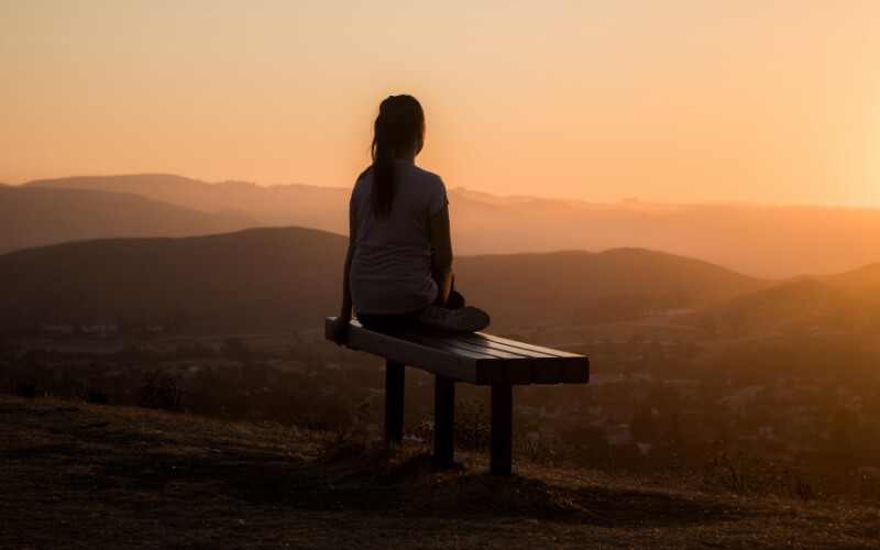 Teenage Girl Sitting on a Bench at Sunset Time